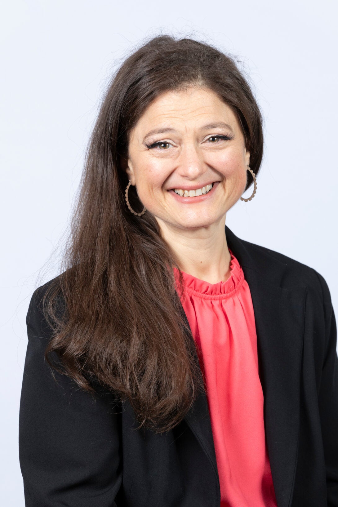 A business headshot of Sherri Ann-Ambrose, who is looking directly at the camera. She is smiling, and wears a black suit jacket with a red undershirt.